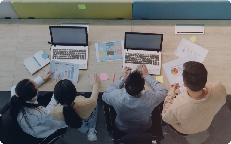 Overhead view of a team working across two laptops and scattered notes