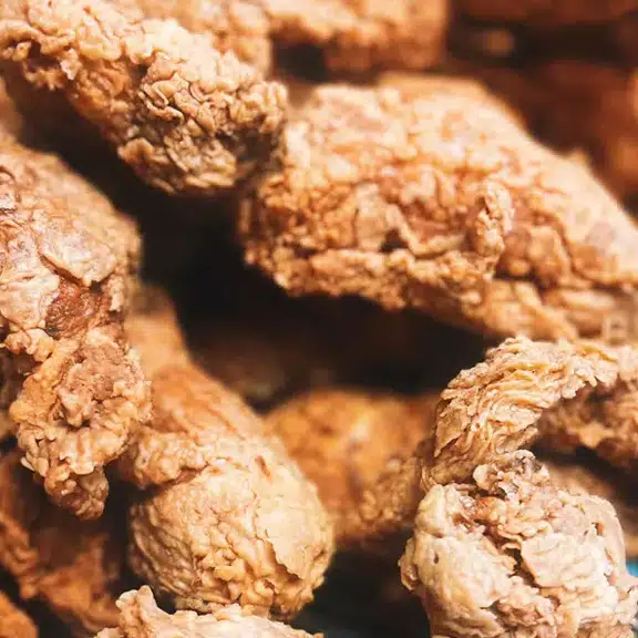 A pile of fried chicken with a close up of a piece of chicken.