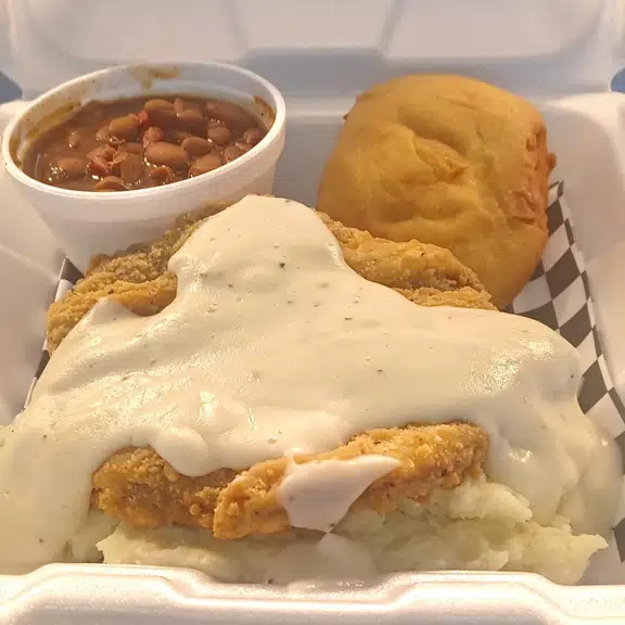 A white styrofoam container with a piece of meat and a biscuit.
