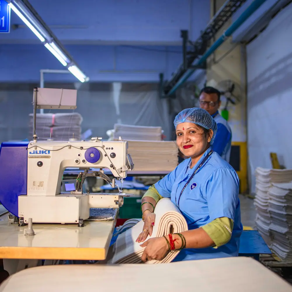 A smiling woman sewing textiles in a factory