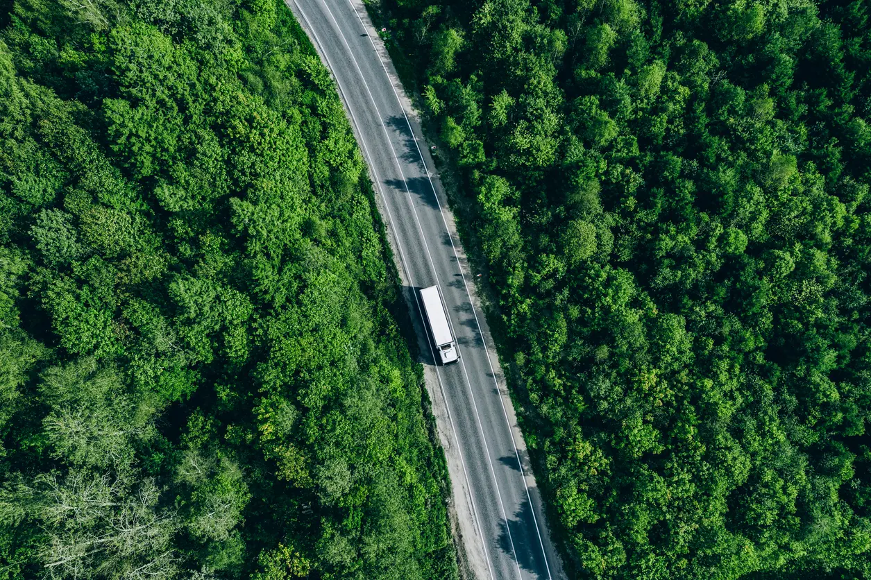 Photo of a semi truck traveling down a highway surrounded by a green forest