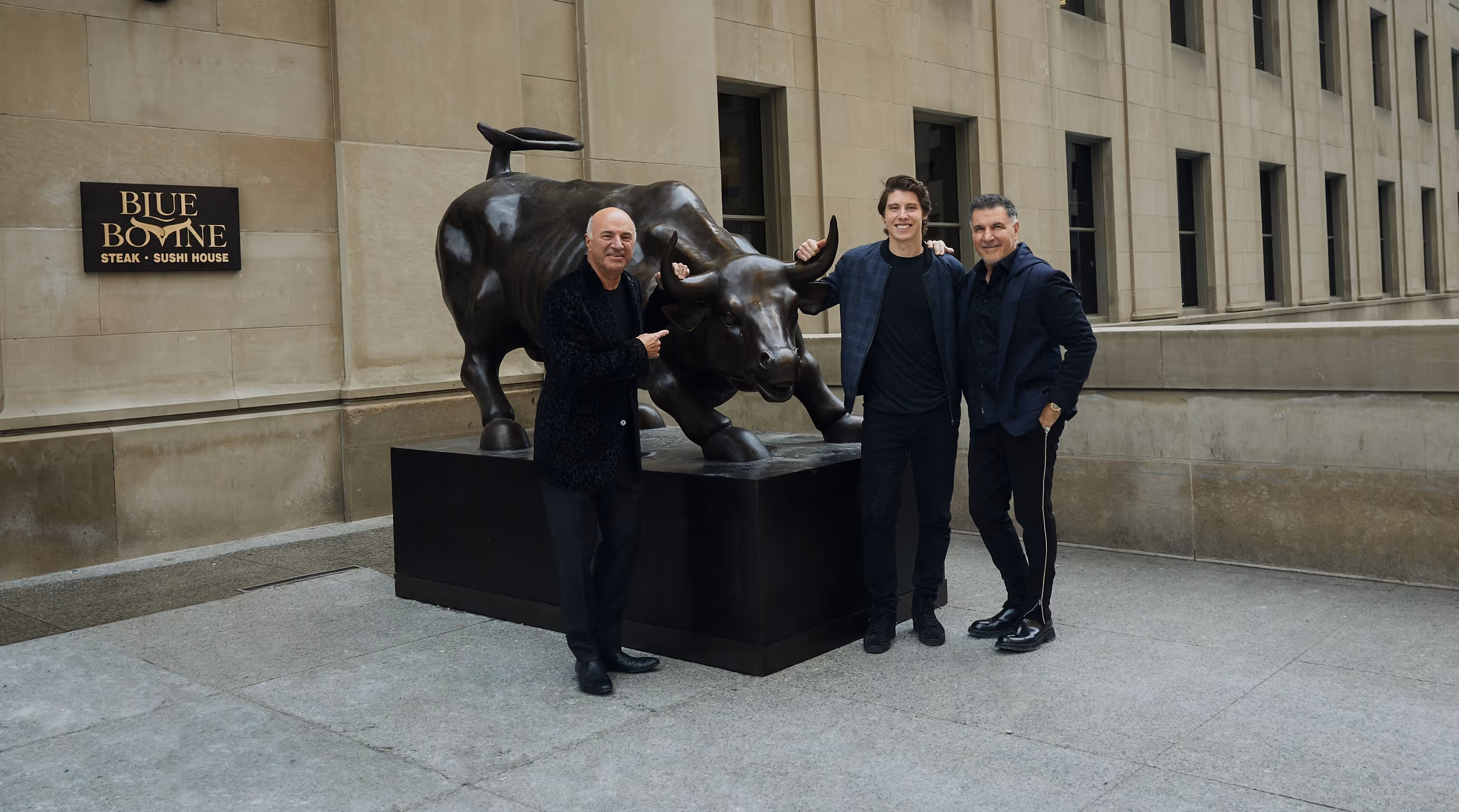 Three men posing around a large bronze bull statue outside a building with a Blue Bovine Steak and Sushi House sign.