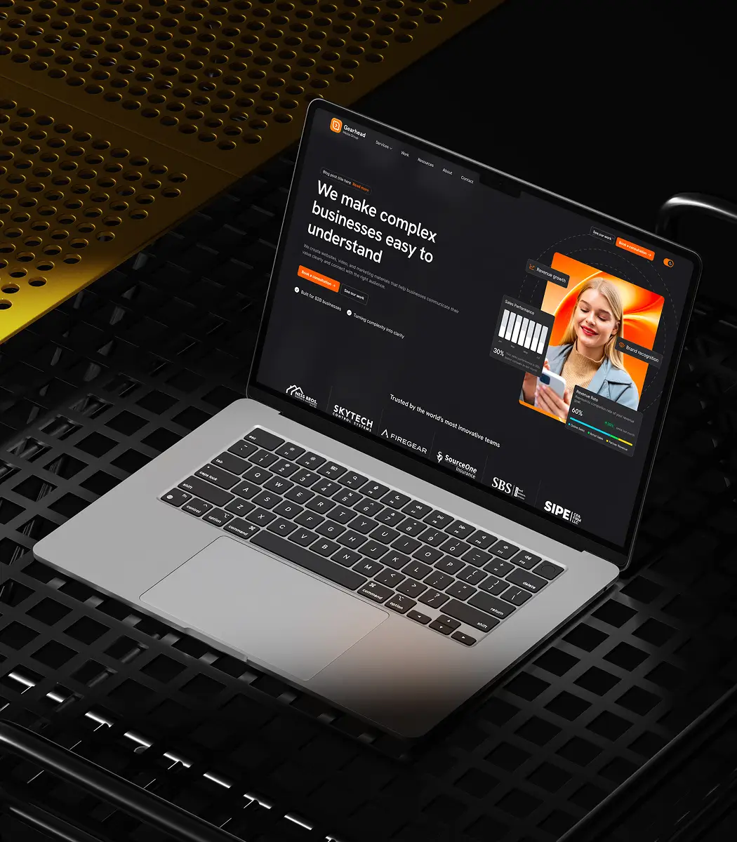 Open laptop on black metal grid surface displaying a website homepage with the headline 'We make complex businesses easy to understand' alongside a photo of a smiling woman and overlay graphics showing sales performance and brand recognition.