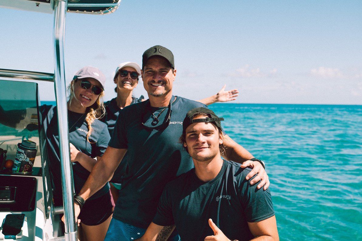 Four people smiling on a boat with the ocean and clear blue sky in the background.