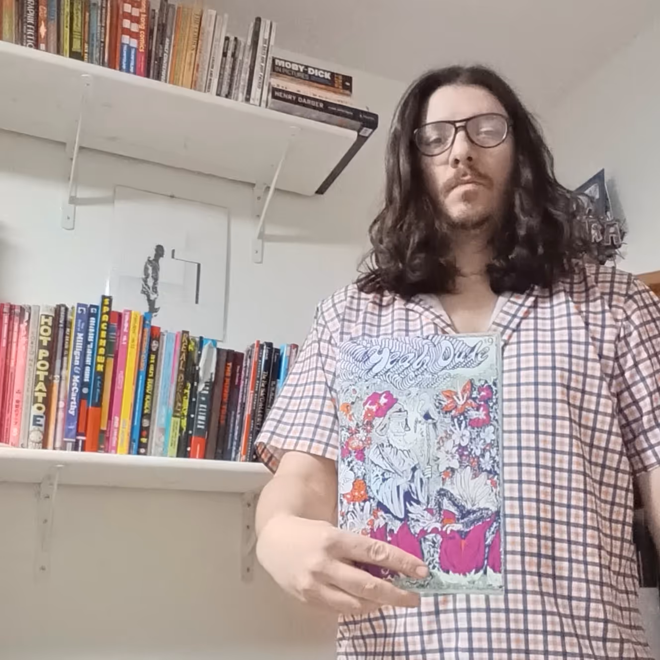 Portrait of a person, facing the camera and holding up a piece of artwork.