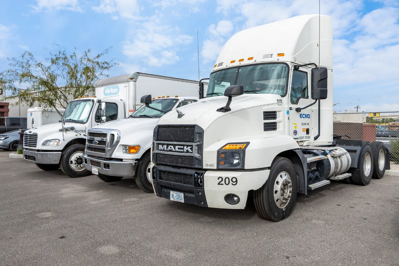 three white heavy-duty trucks, lead cab bears bold MACK grille, lined up for yard maintenance.