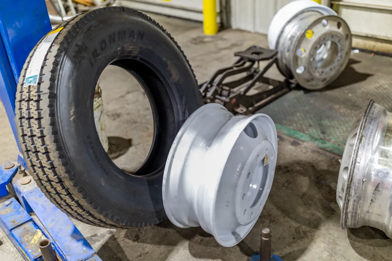 Tire replacement setup with IRONMAN truck tire and multiple steel rims on a shop floor.