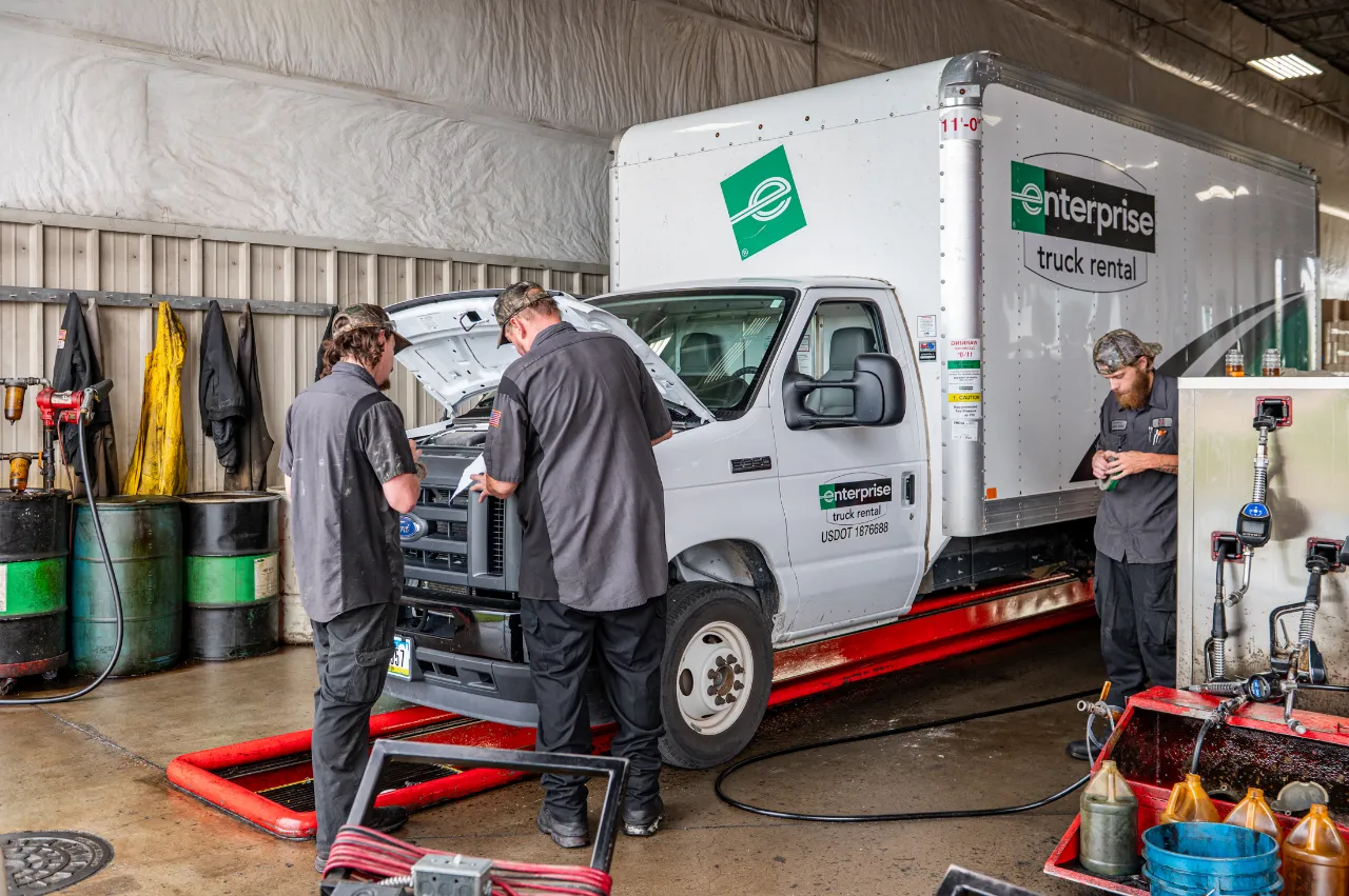 Technicians performing truck maintenance on an Enterprise box truck inside a heavy-duty repair shop.