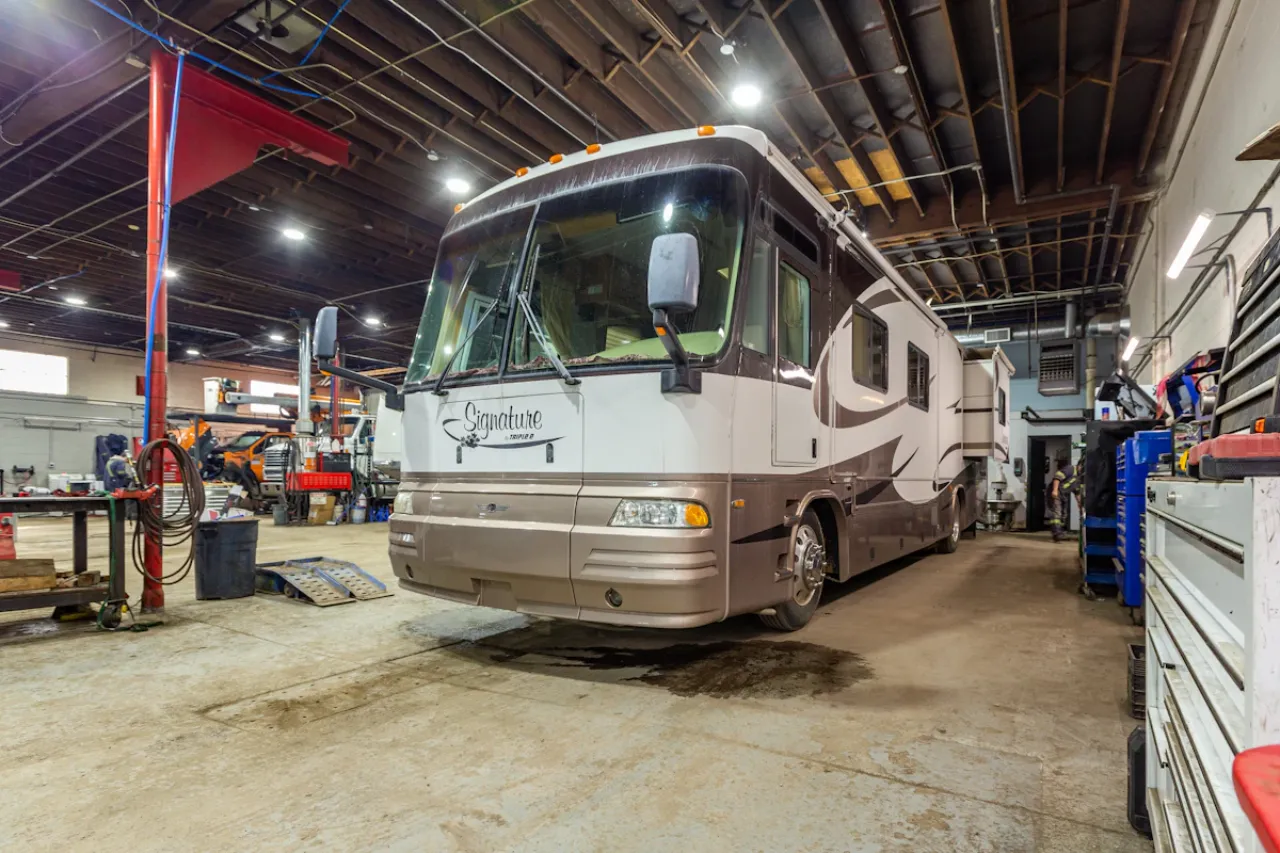RV repair on Signature motorhome inside heavy-duty shop with tools, lift equipment, and open ceiling workspace.