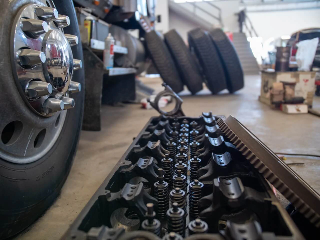 Tires service showing heavy-duty wheel and exposed engine cylinder head with valves and springs on shop floor.