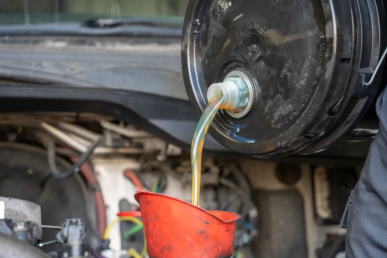 Oil and fluid service on a heavy-duty truck with fluid draining into a red funnel during maintenance.