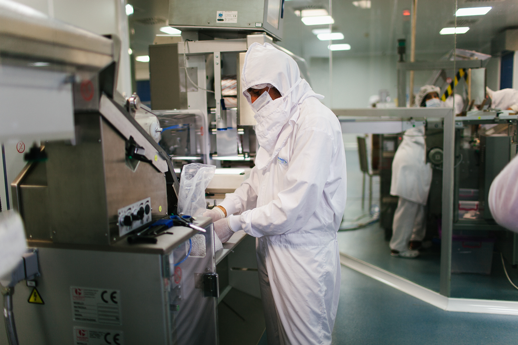 Worker in full protective suit handling materials near packaging machinery in a sterile factory environment.