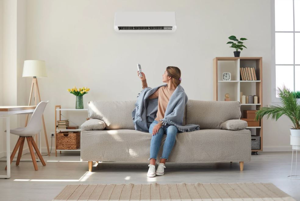 Woman using remote to control wall-mounted air conditioner in living room.