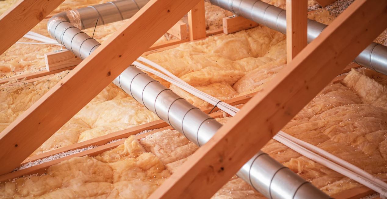 Attic with insulation and metal air ducts installed between wooden beams.