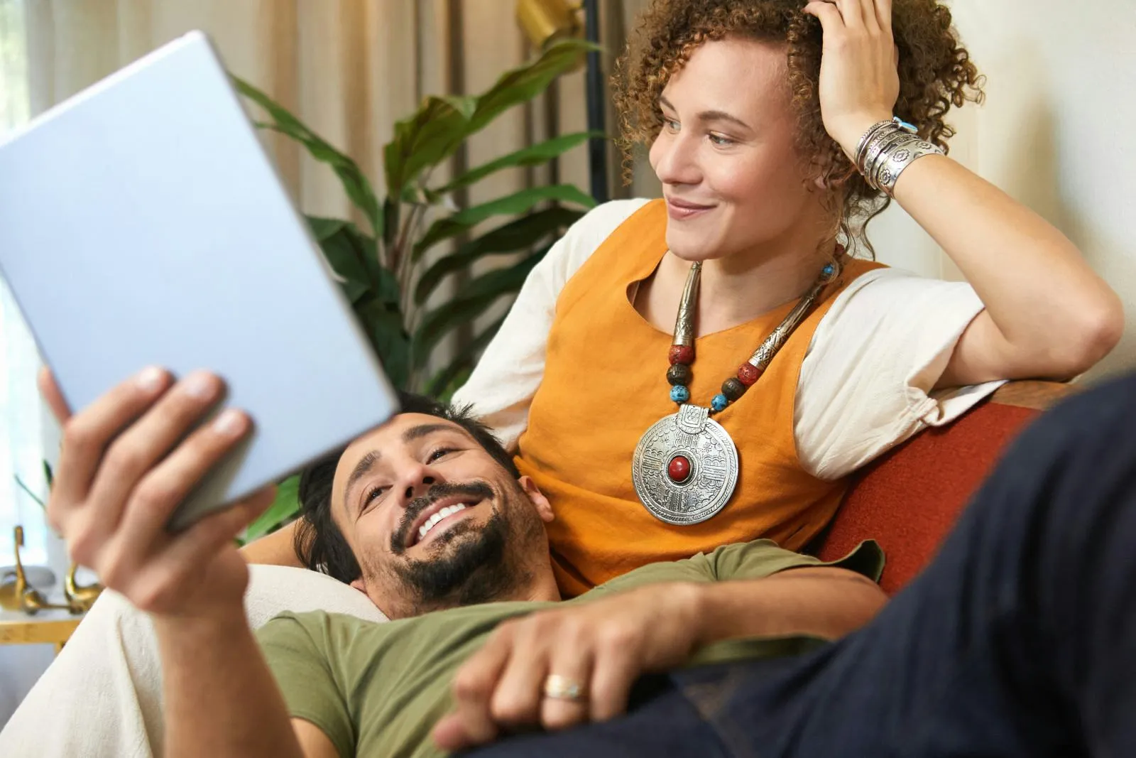 Smiling couple relaxing on a couch, looking at a digital tablet together