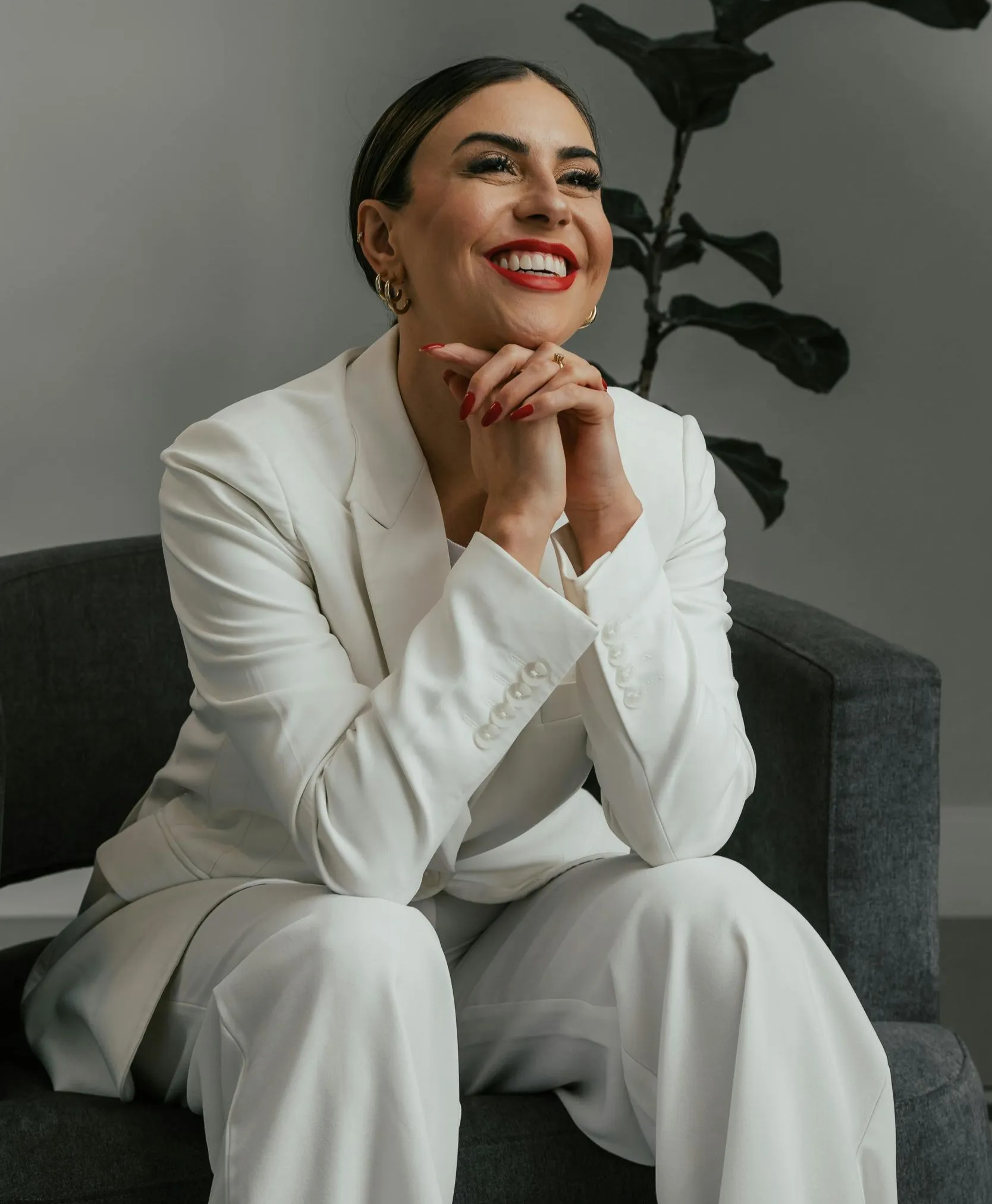 Confident woman in a white suit smiling while seated in a modern office setting