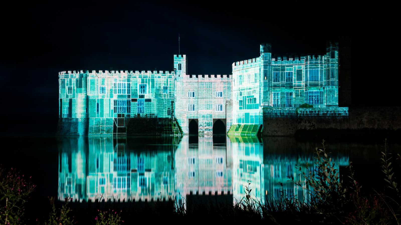 Nighttime projection of a classical building lit with blue and green lights over water