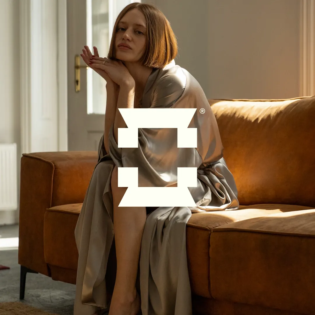 Blonde female model in a satin robe sitting in a living room, posing elegantly with her hands crossed as background image for Celedon imagery logo.