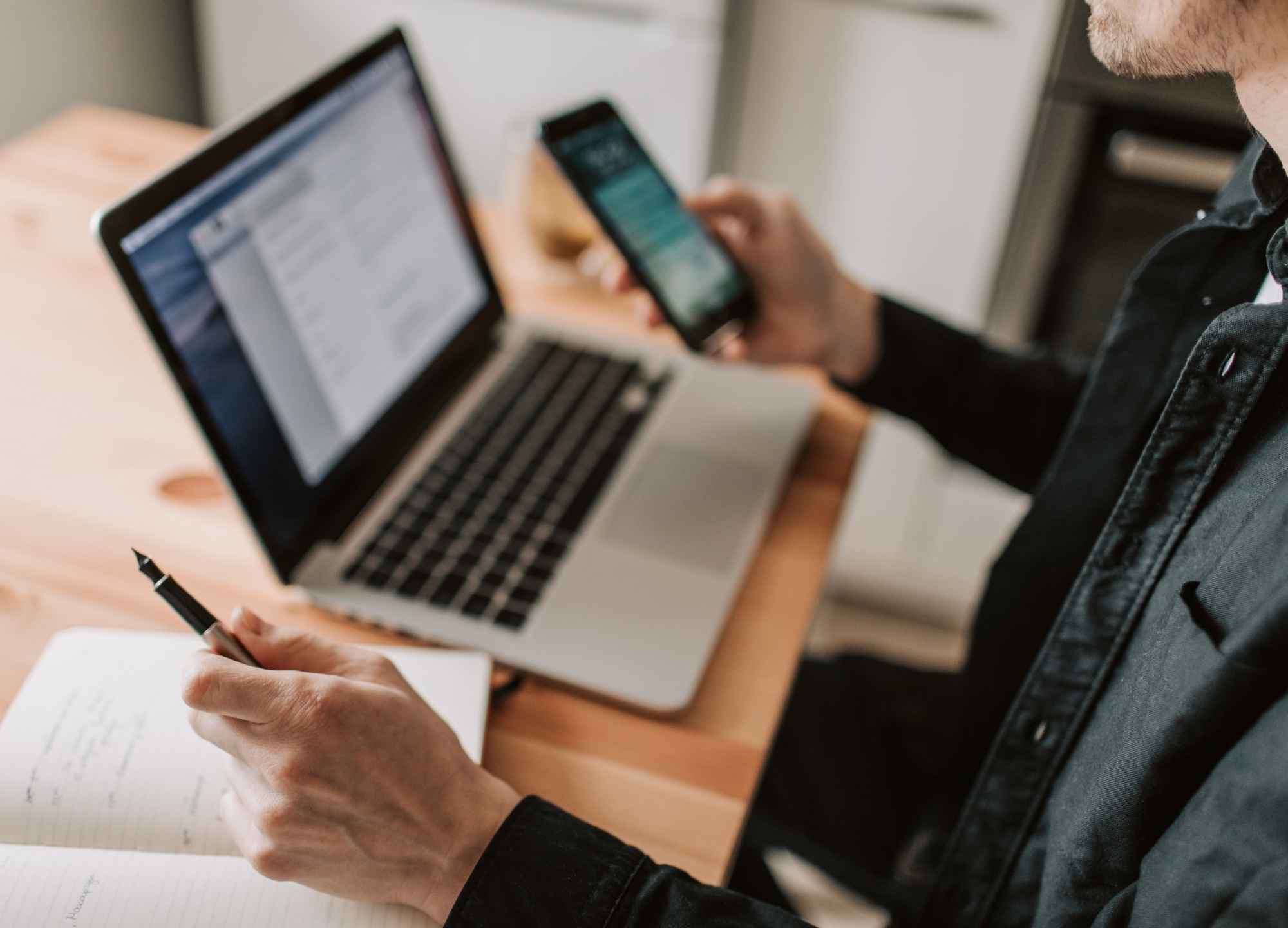 Profissional usando notebook e celular ao mesmo tempo durante atendimento via WhatsApp
