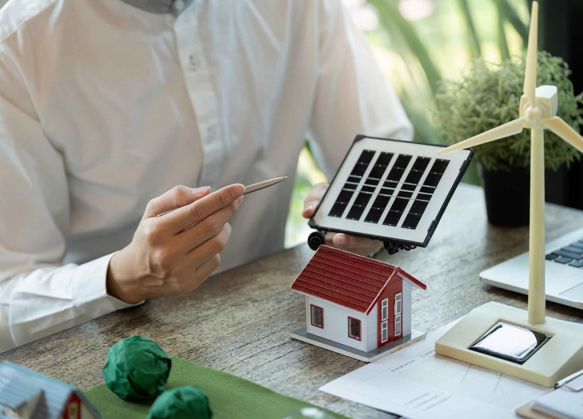 Profissional apresentando projeto solar com maquete de casa e mini painel fotovoltaico