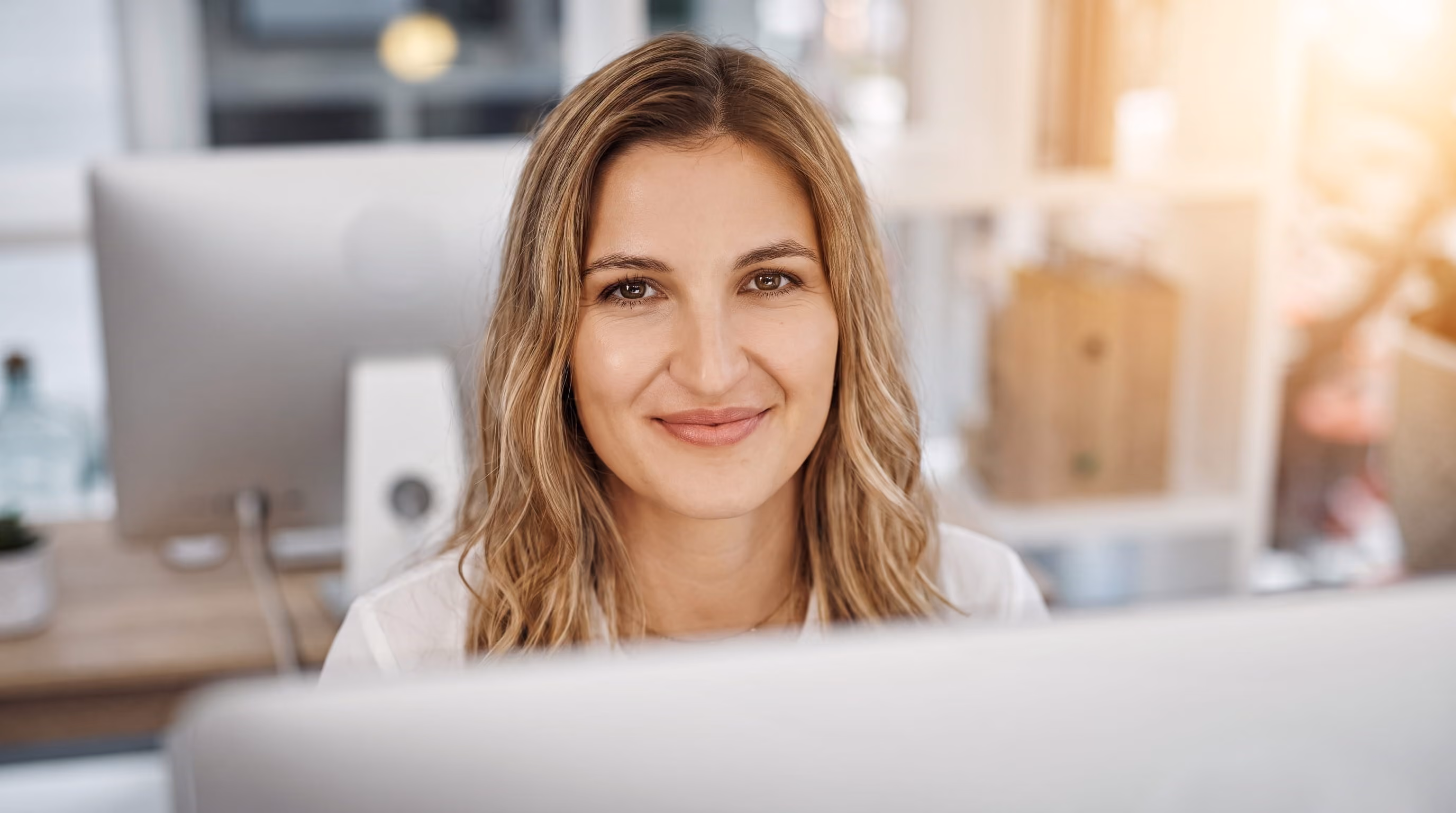 Frau mit langen blonden Haaren arbeitet konzentriert an einem Computer in hellem Büro.