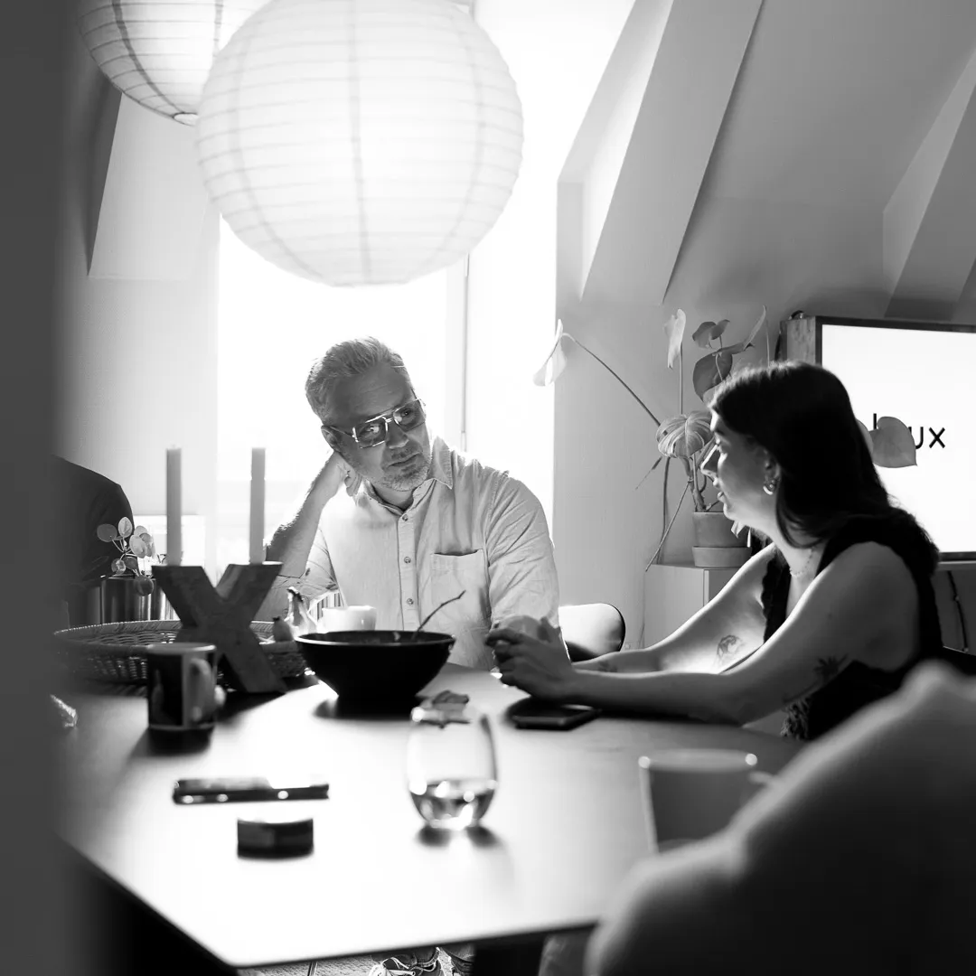 Två personer sitter vid ett mötesbord och samtalar i ett ljust kontor med avslappnad stämning.