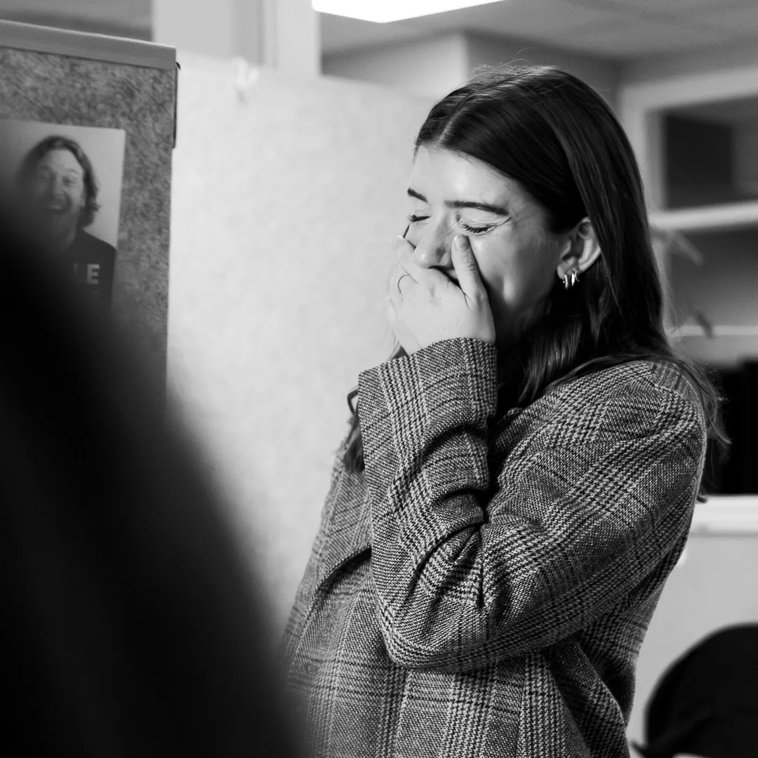 Person skrattar och håller handen för munnen i en kontorsmiljö, fångad i ett spontant ögonblick.