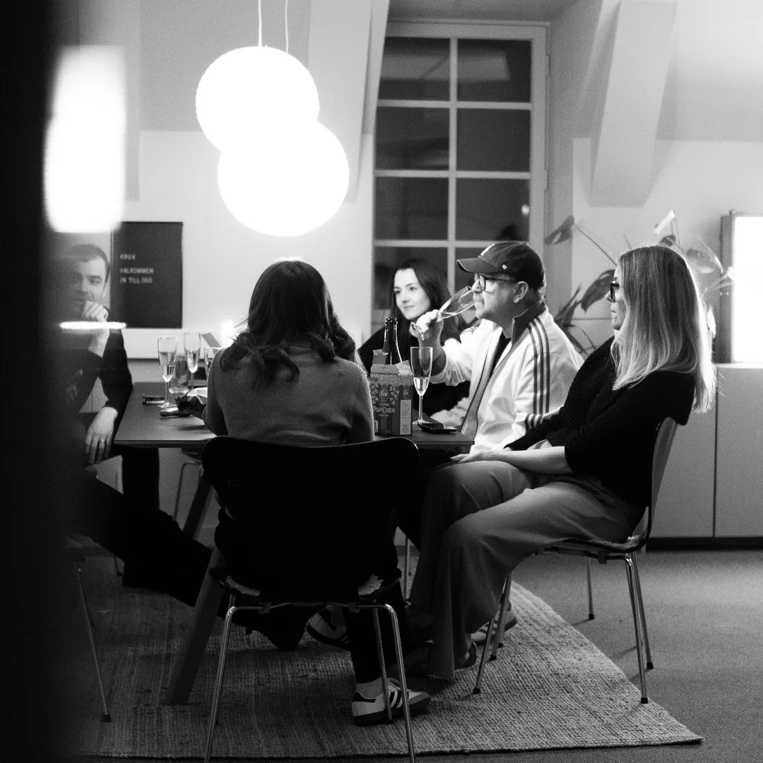 Två personer står och kramas leende i en kontorsmiljö med skrivbord i bakgrunden.