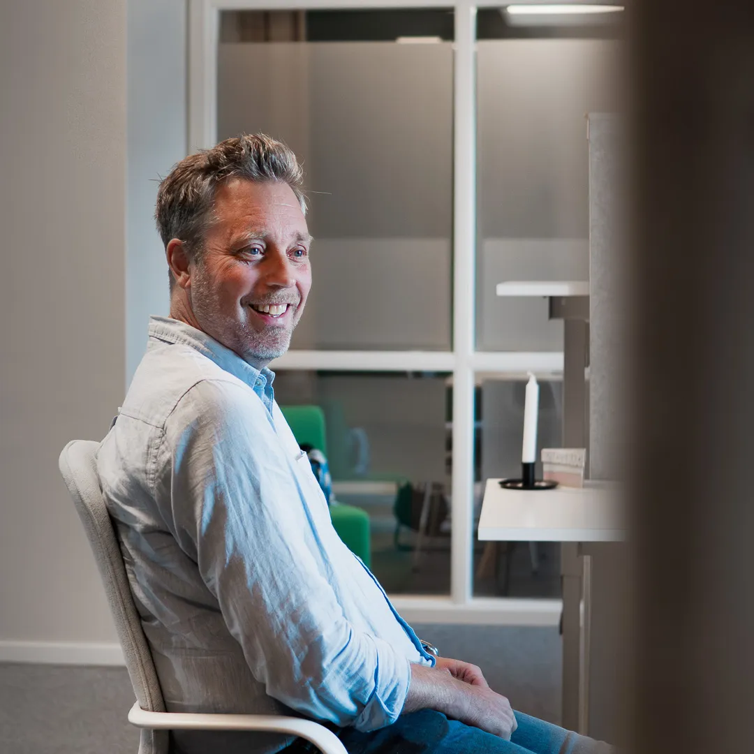 Person sitter på en stol, tittar snett mot kameran och ler