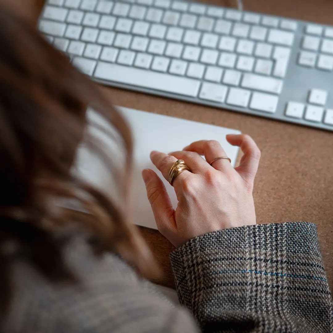 Närbild av en person som arbetar vid dator, handen på styrplatta framför ett tangentbord.