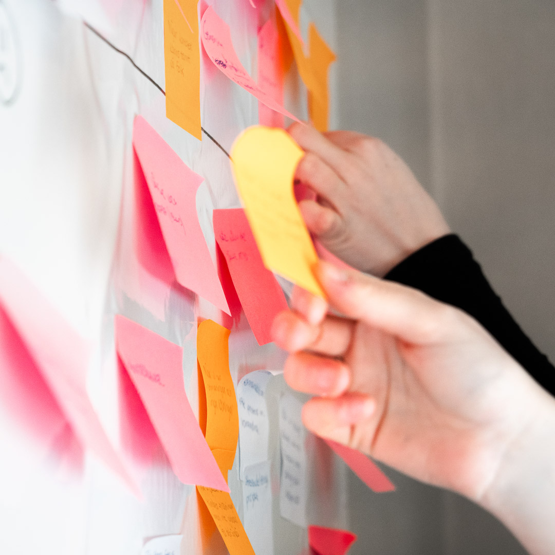 Person sitter vid ett bord och observerar en grupp kollegor som samarbetar runt ett bord i ett mötesrum.