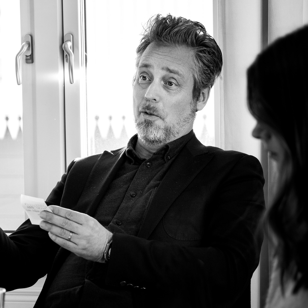 Person med glasögon sitter vid en laptop och pekar på skärmen under ett samtal eller samarbete.