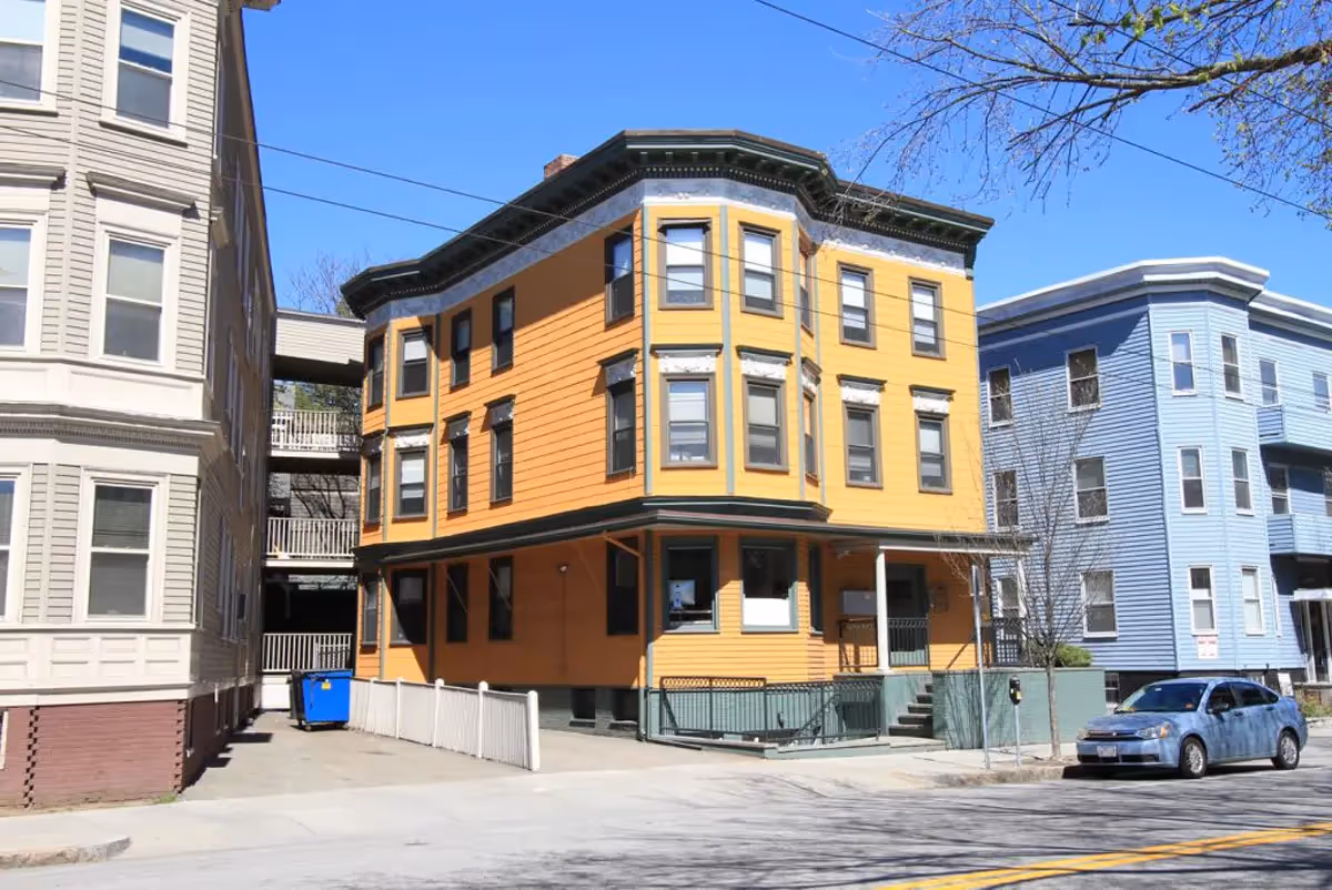 Small, early-to-mid 1900s, three-story apartment building with yellow siding and green trim