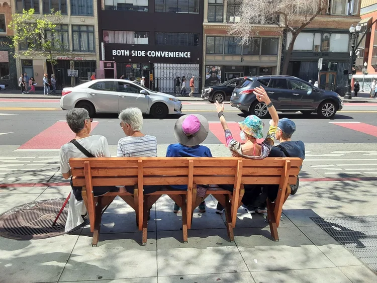 People sitting on a handmade bus bench on the sidewalk