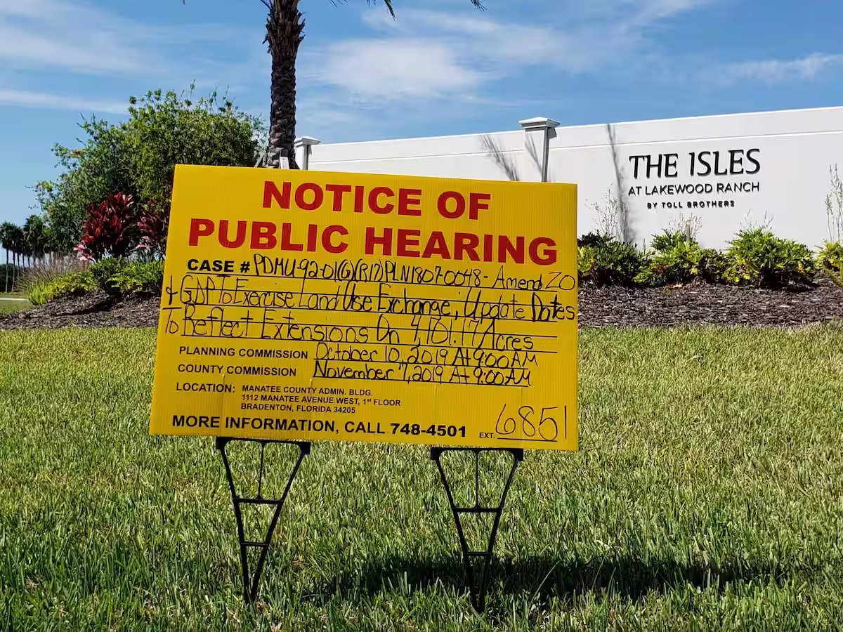 Yellow lawn sign saying notice of public hearing with the details scrawled on in marker