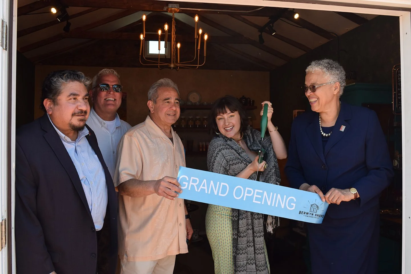 Shop owners cut a ribbon that says "Grand Opening."
