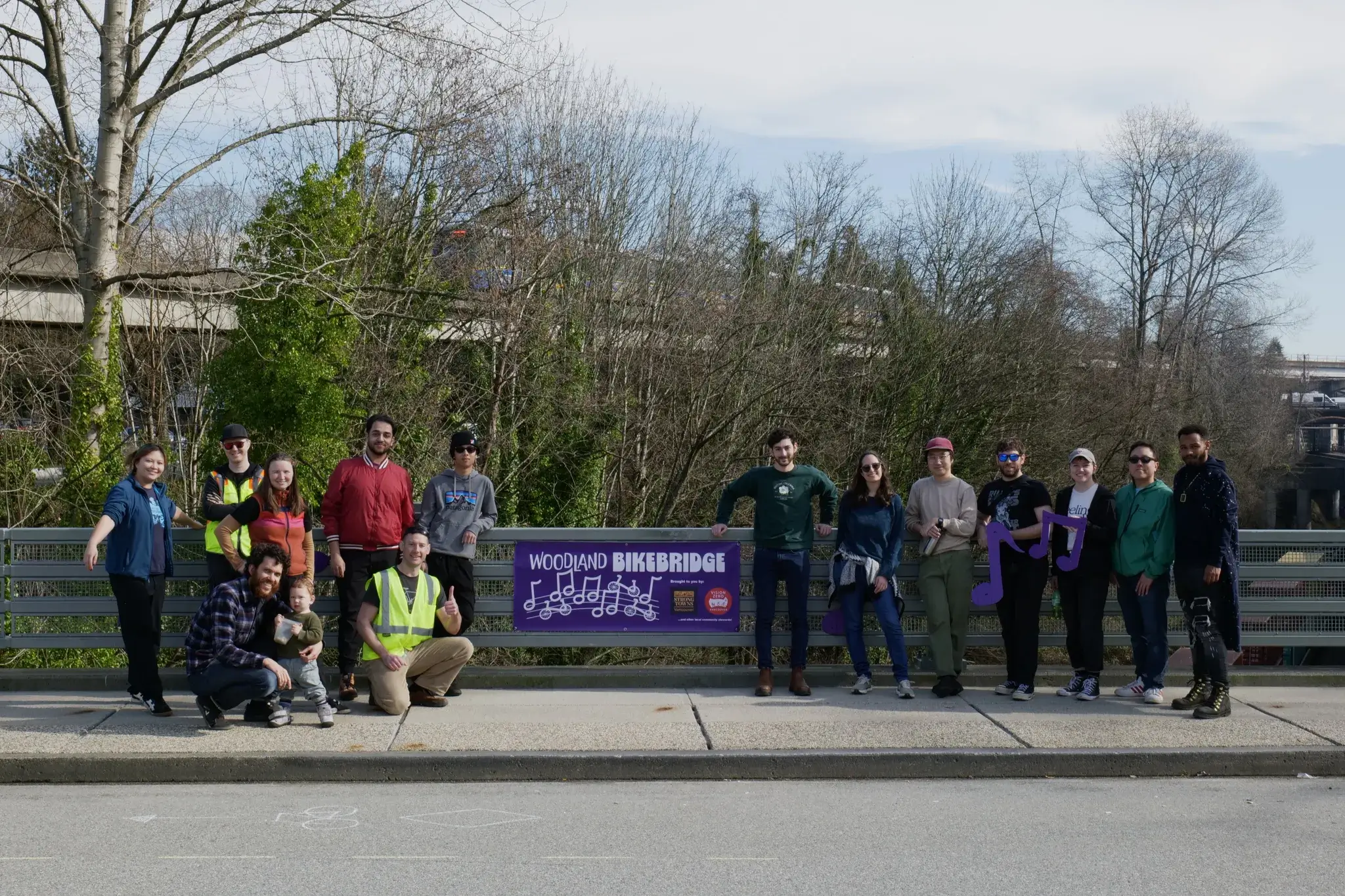 Strong Towns Vancouver and Vision Zero Vancouver volunteers, local residents and curious visitors pose for a photo in front of the Woodland BikeBridge banner on setup day