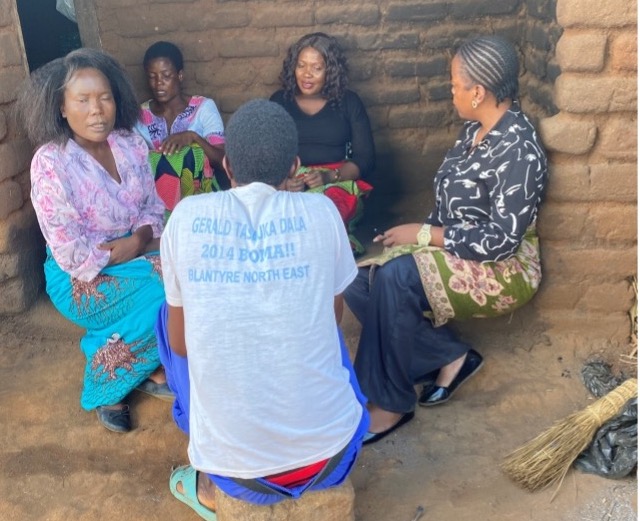 Women gather in a mud-walled room for a community meeting
