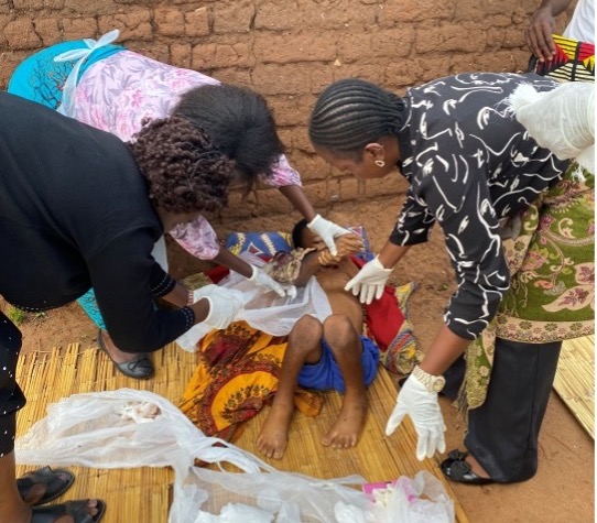 Medical workers treating a child on a mat outdoors