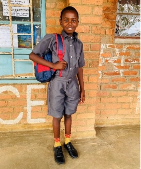 Schoolboy in gray uniform stands with red backpack near brick wall