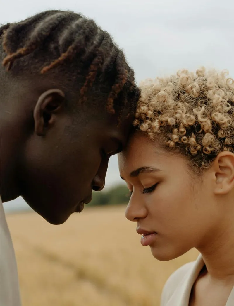 A young couple stands in a field, eyes closed, enjoying a serene moment together amidst nature.