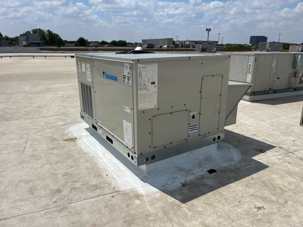 Daikin rooftop HVAC unit installed on a flat roof under a partly cloudy sky.