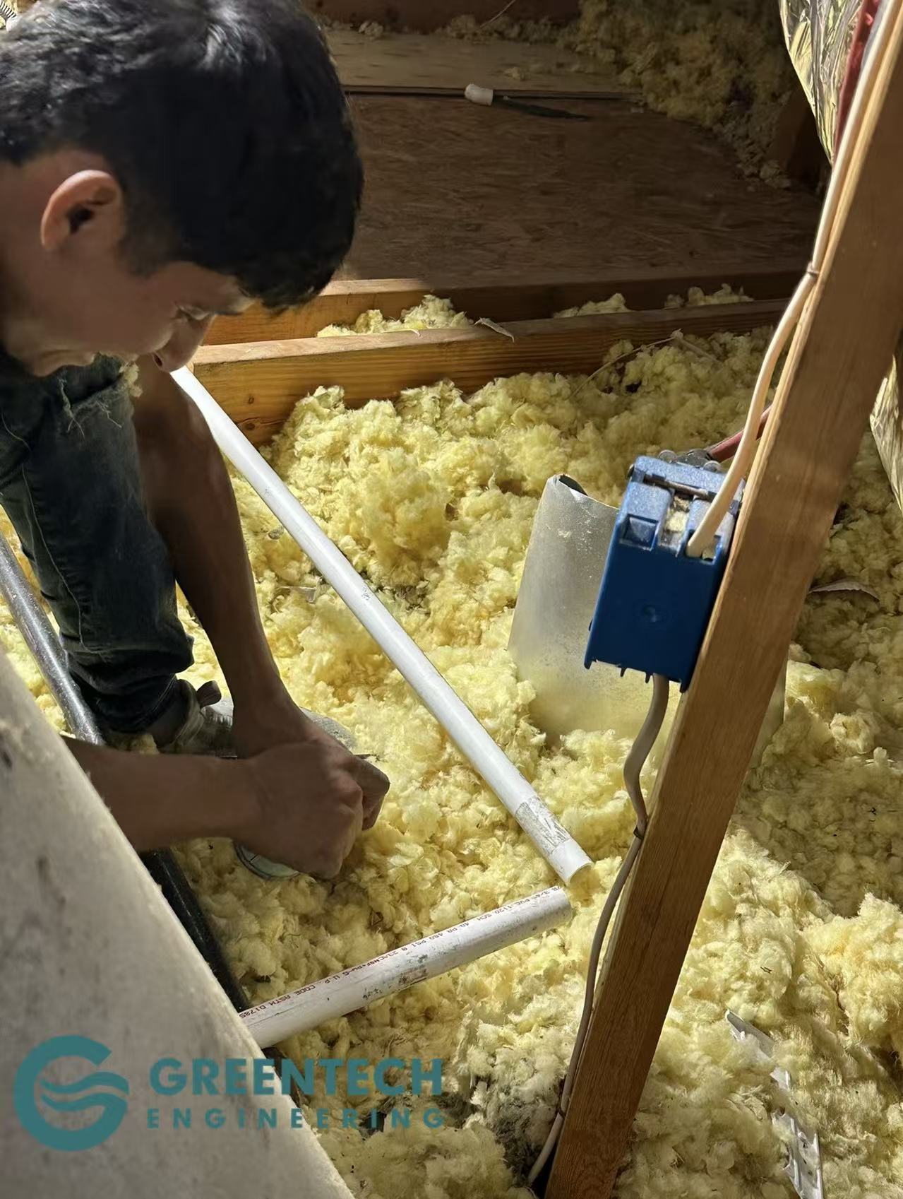Professional HVAC technician cutting and repairing a clogged AC PVC drain pipe in a residential attic.