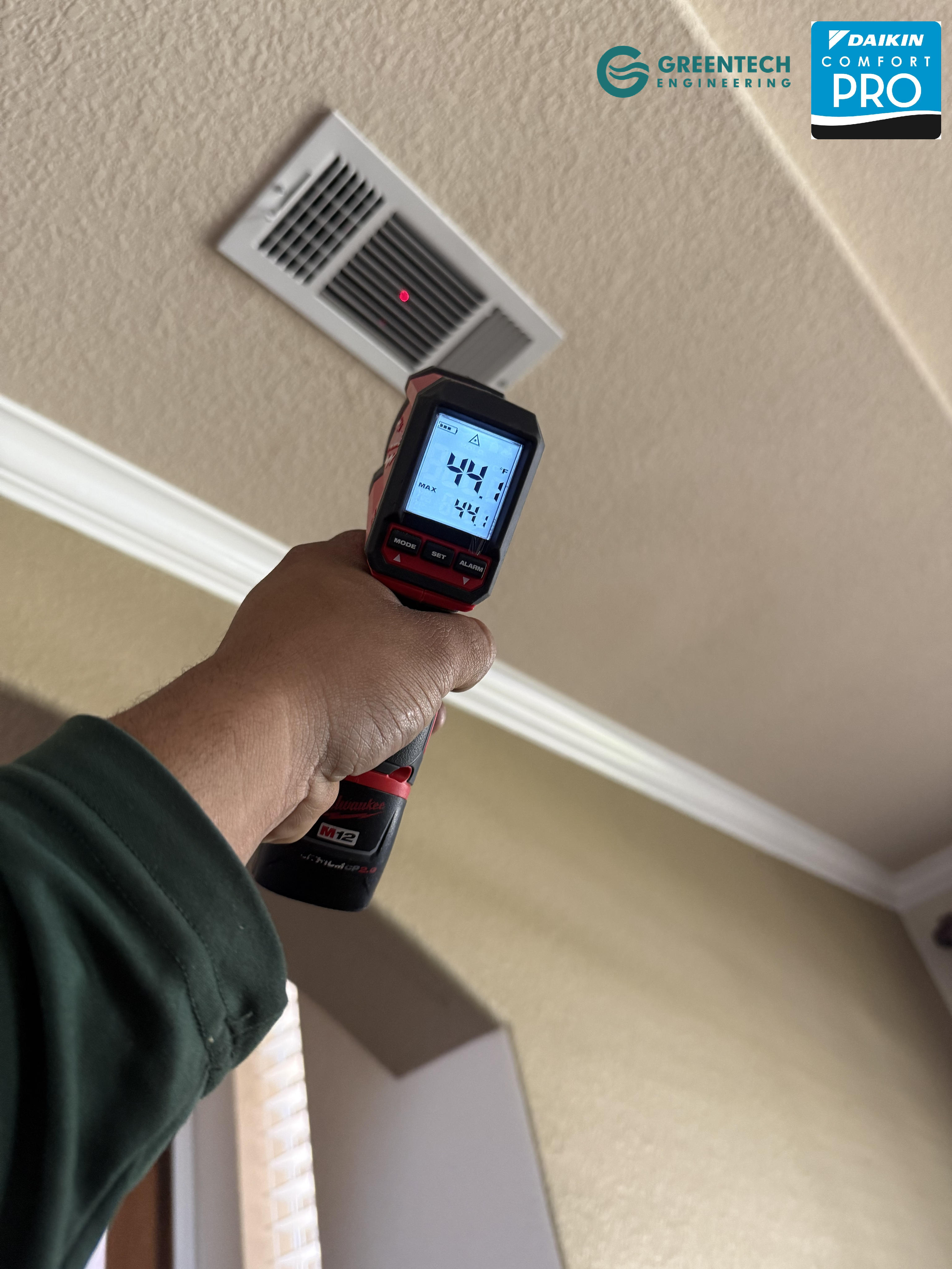 Technician holding a digital infrared thermometer pointing at a ceiling vent, reading 44.1 degrees Fahrenheit.