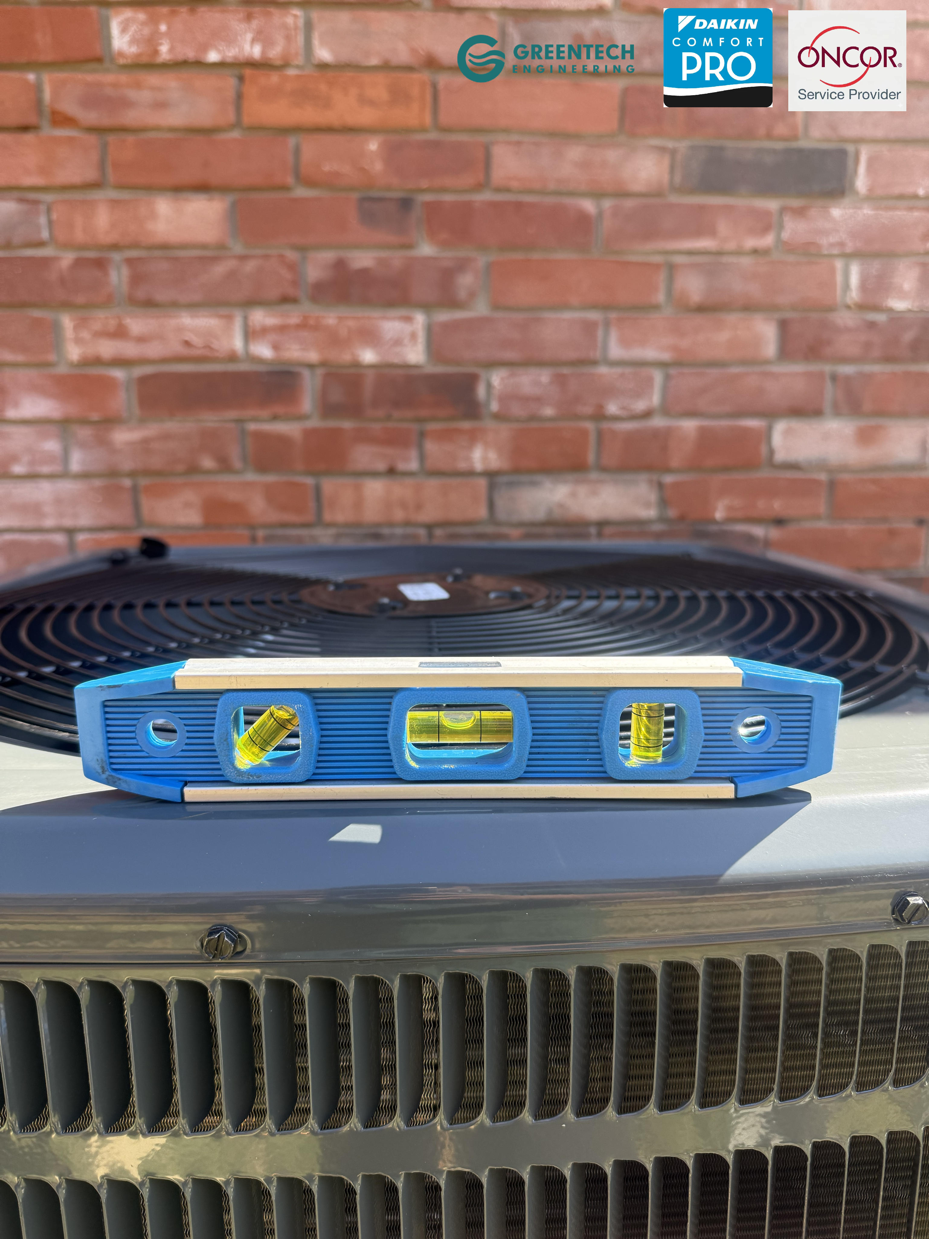 A precision spirit level sitting on top of a newly installed Goodman AC condenser to ensure perfect balance on a new concrete pad.