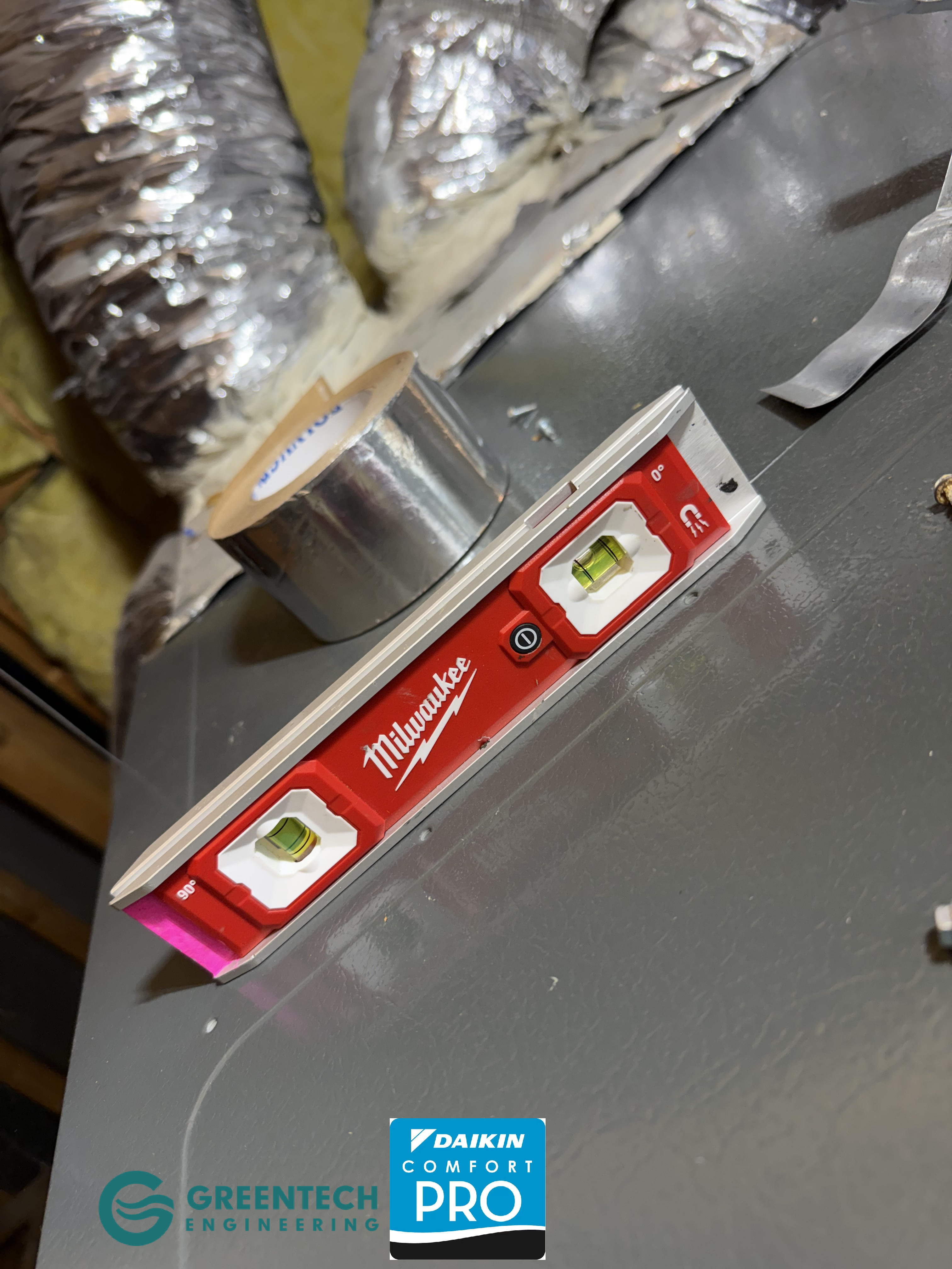 A red Milwaukee magnetic level resting on a newly installed grey HVAC furnace cabinet in an attic to ensure perfect horizontal alignment.