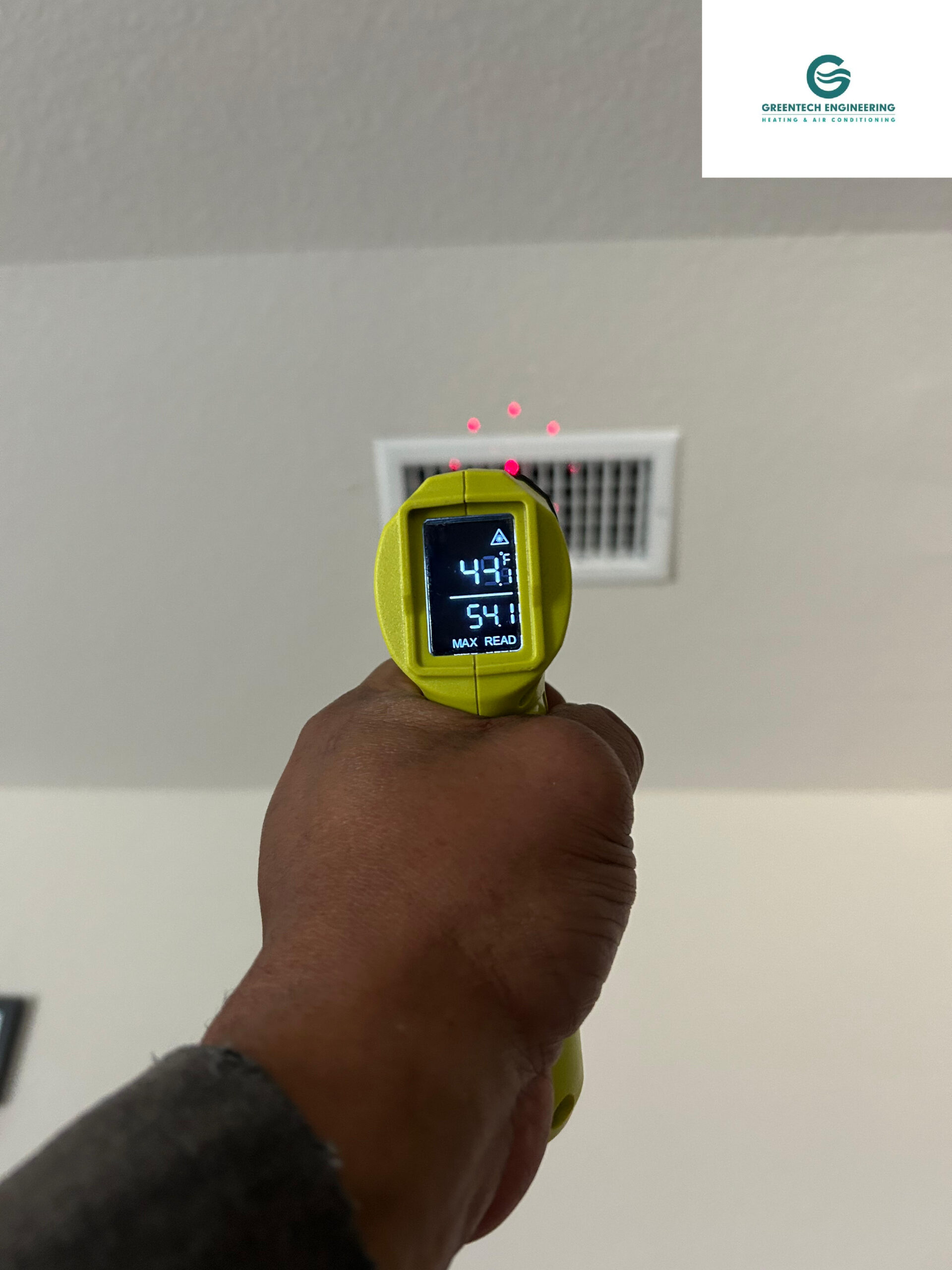 Greentech Engineering technician using a laser thermometer to measure 54°F cold air blowing from a ceiling vent after a successful AC repair in Grand Prairie, TX.