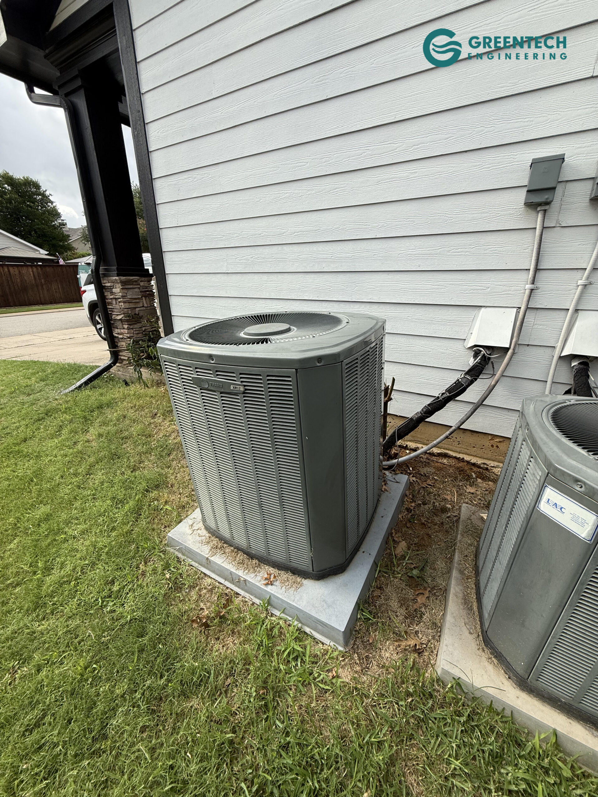 An aging, low-efficiency Trane air conditioning condenser sitting in the grass outside a residential home in Allen, Texas.