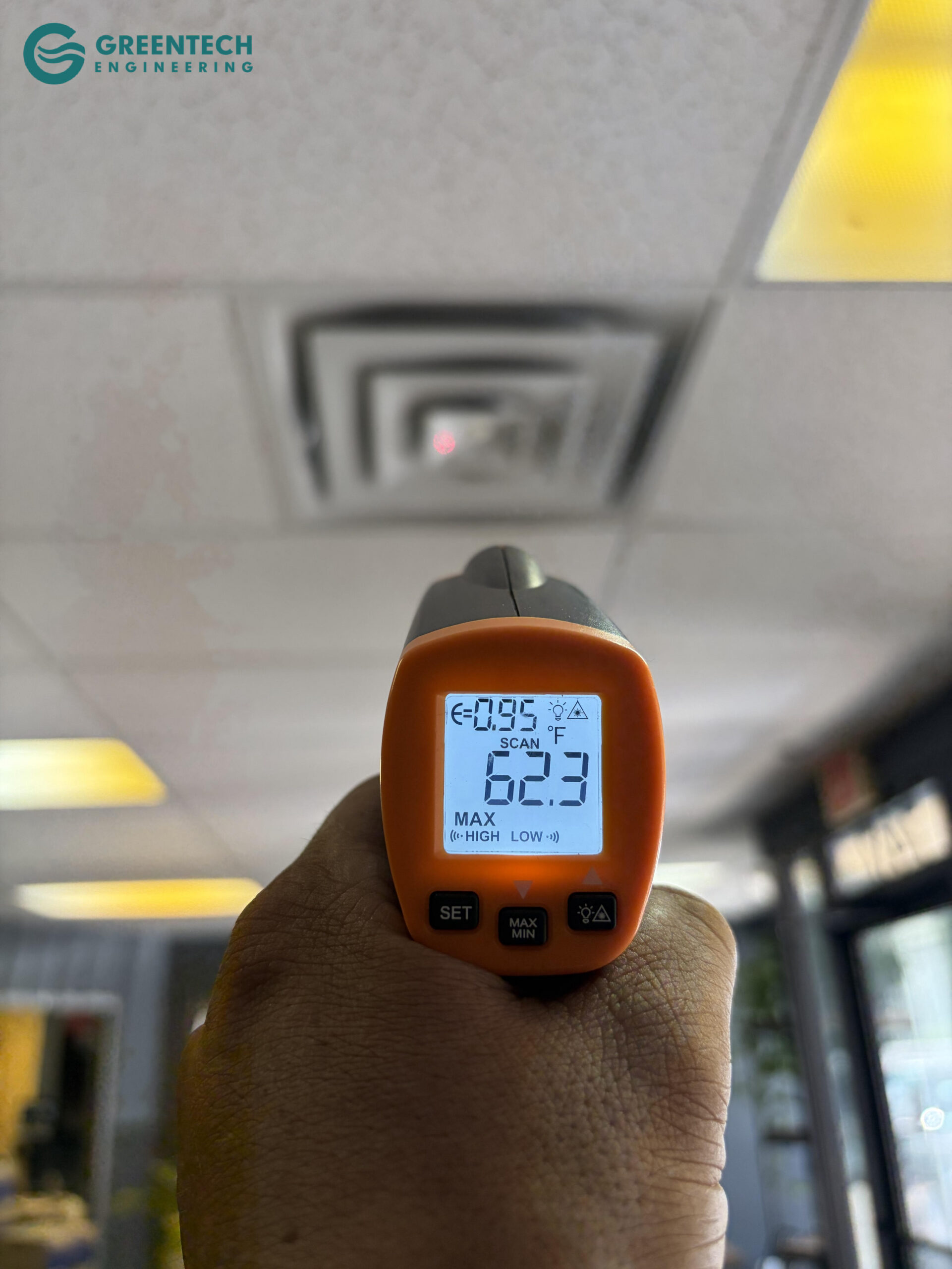A digital infrared thermometer pointing at a commercial office drop-ceiling vent, registering a frosty 62.3 degrees Fahrenheit.