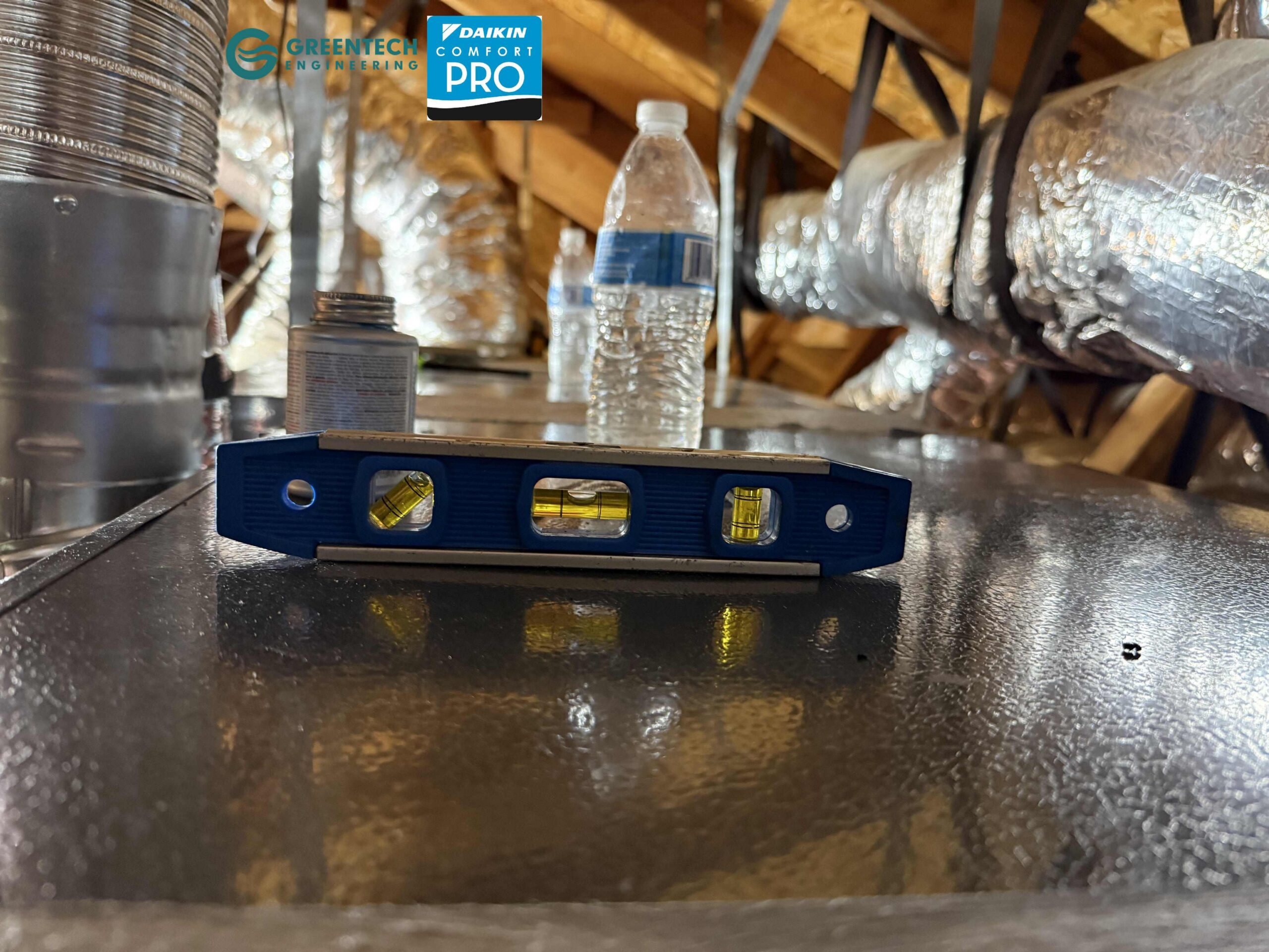 A blue torpedo level sitting on top of a newly installed Daikin horizontal evaporator coil in an attic to ensure perfect pitch for the condensation drain pan.